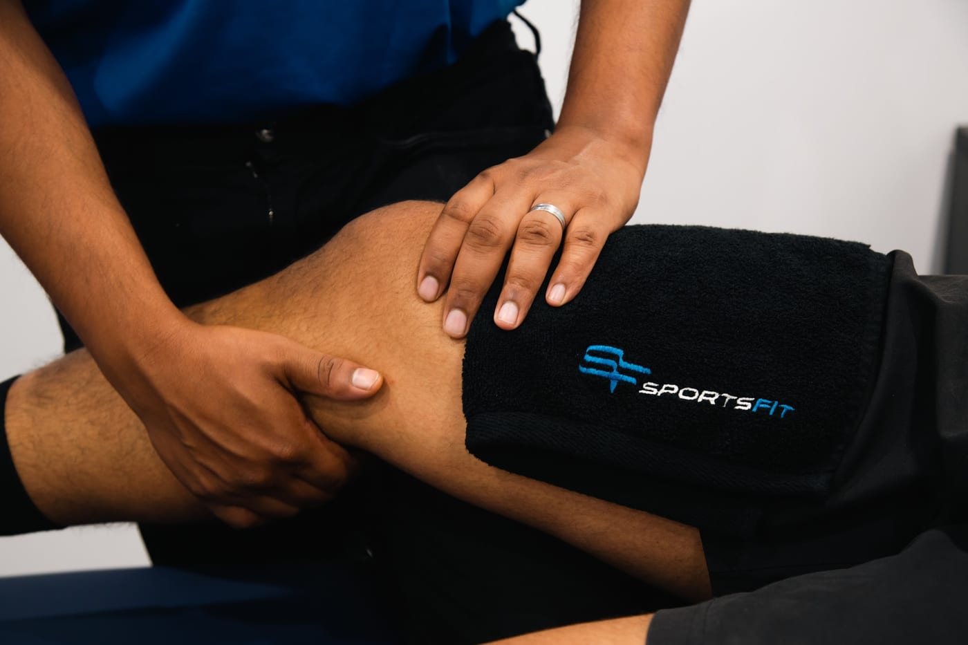 A practitioner's hands assessing a patient's knee over a SportsFit towel
